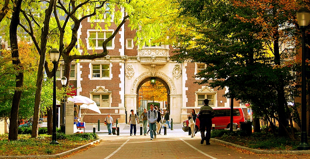 Students walk under an archway on a college campus in the fall.