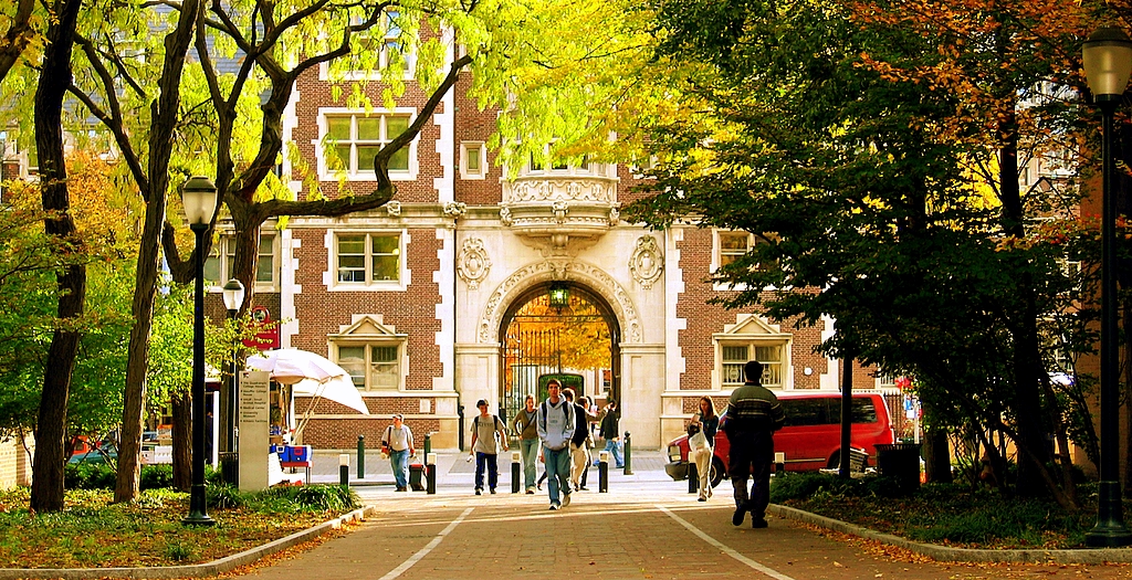 Students walk under an archway on a college campus in the fall.